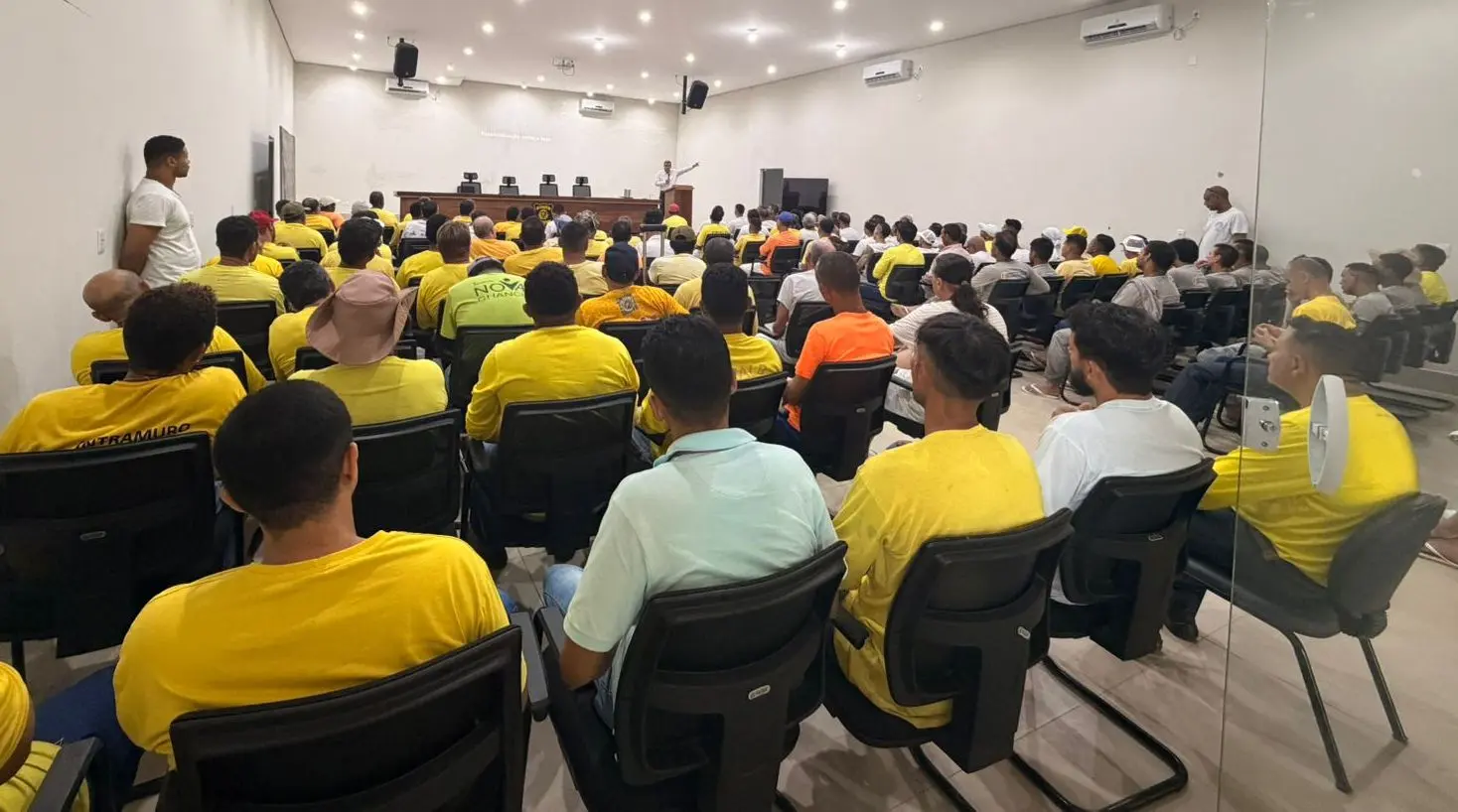Foto horizontal que mostra o auditório do presídio Ahmenon Lemos Dantas lotado de recuperandos, que aparecem de costas na foto, usando uniforme amarelo.