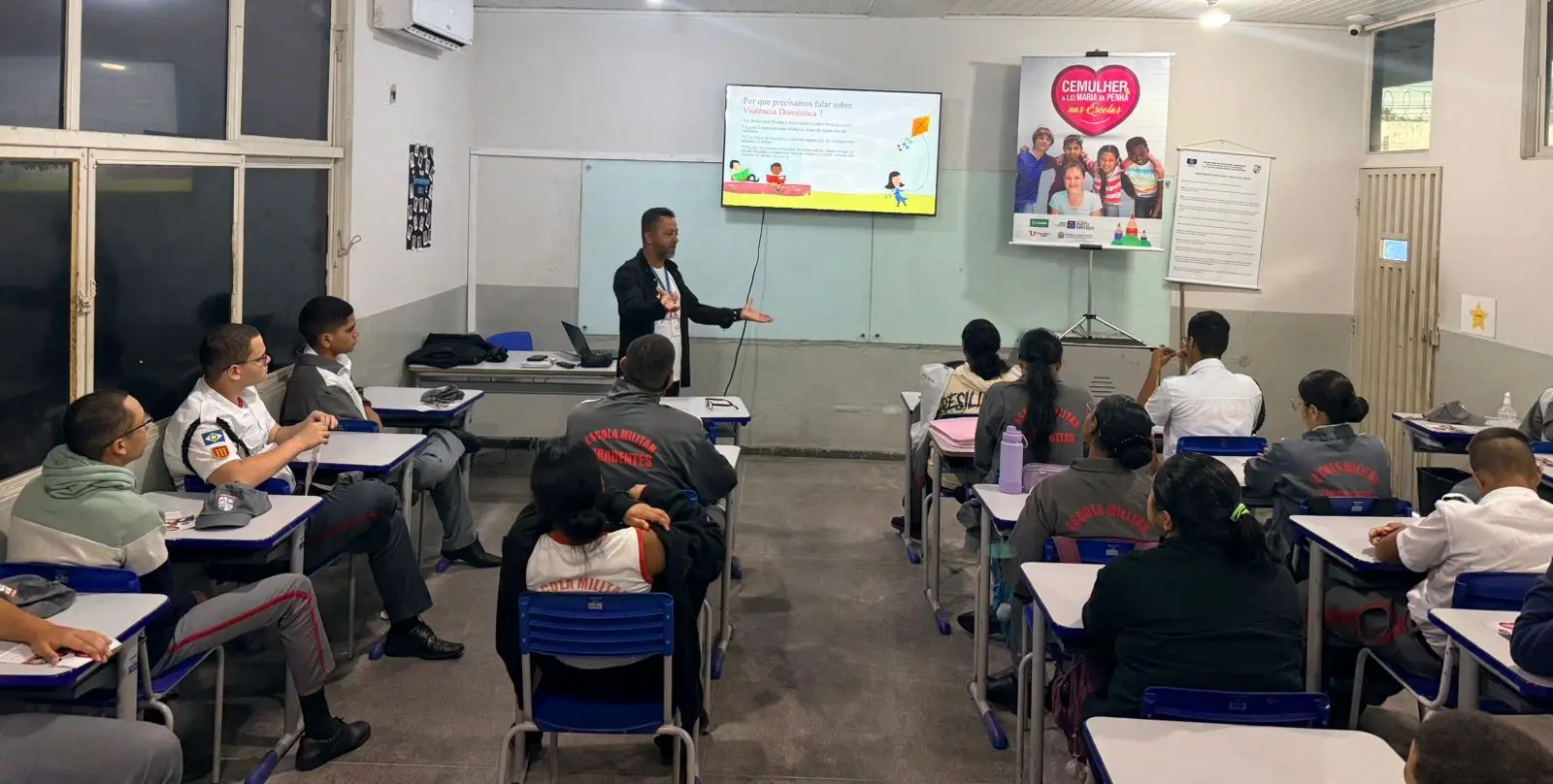 Foto horizontal em plano aberto que mostra uma sala de aula com alunos ouvindo a palestra do servidor Cristian Pereira, da Cemulher.